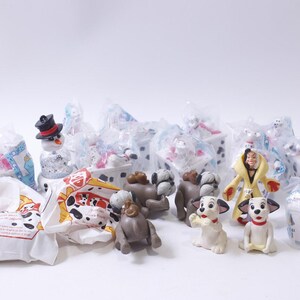 Könnte beinhalten: Eine Sammlung von 101 Dalmatiner-Spielzeug und Verpackungen. Zu den Spielzeugen gehören ein Schneemann, ein Dalmatiner-Welpe, Cruella de Vil und ein Dalmatiner-Hund. Die Verpackung besteht aus durchsichtigem Plastik und trägt das 101 Dalmatiner-Logo.