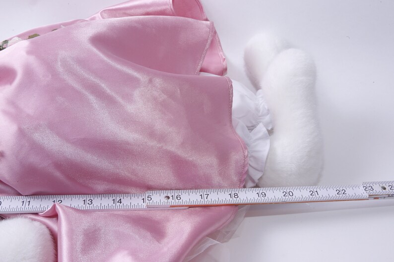 Peut inclure: Une robe en satin rose avec une bordure en dentelle blanche et une queue en fourrure blanche. La robe est mesur&eacute;e avec une r&egrave;gle, montrant une longueur de 50,8 cm.
