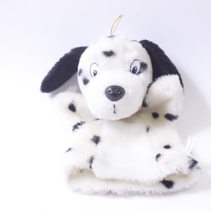 Puede incluir: Títere de perro dálmata de peluche con manchas negras sobre un fondo blanco. El títere tiene orejas negras, una nariz negra y un hilo dorado sujeto a la parte superior de la cabeza. El títere está hecho de material suave y esponjoso.