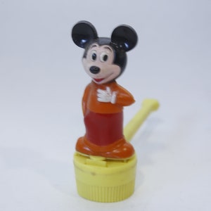 May include: A vintage Mickey Mouse figure, featuring black ears, a red and orange outfit, and white gloves. The figure is mounted on a yellow base with a yellow tube extending from the side. A classic Disney collectible.