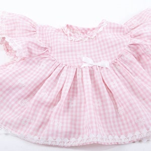 May include: A pink and white gingham baby dress with white lace trim and a white bow at the waist.