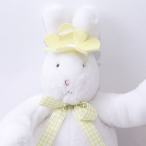 May include: White plush bunny with yellow flower on its head and a green and white checkered ribbon around its neck.