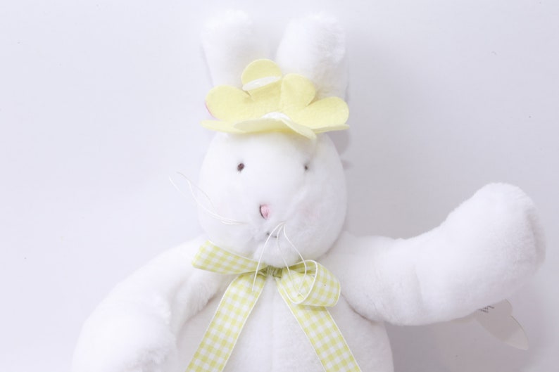 May include: White plush bunny with yellow flower on its head and a green and white checkered ribbon around its neck.