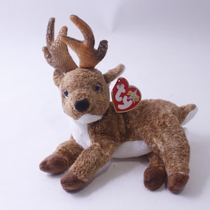Puede incluir: Un reno de peluche marrón y blanco con grandes cuernos. El reno está tumbado con la cabeza girada hacia un lado. Tiene una etiqueta Ty roja y blanca pegada en la espalda.
