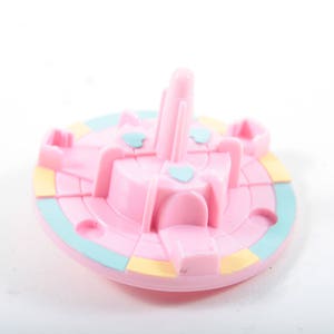 May include: A pink plastic carousel with a blue and yellow base. The carousel has four horses and a center pole.