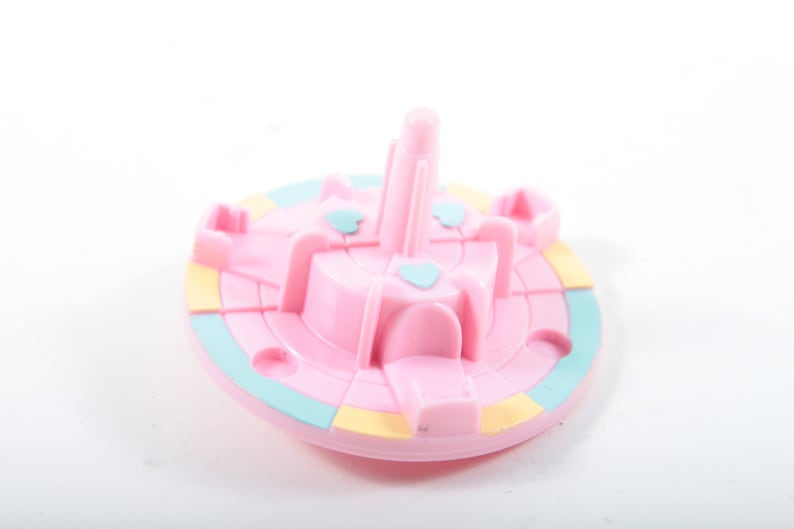 May include: A pink plastic carousel with a blue and yellow base. The carousel has four horses and a center pole.