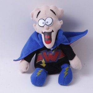 May include: A plush toy of a character with a large head, wide eyes, and a big smile. The character is wearing a blue cape, a black shirt with a red and yellow 'W' on it, and blue boots with yellow lightning bolts.