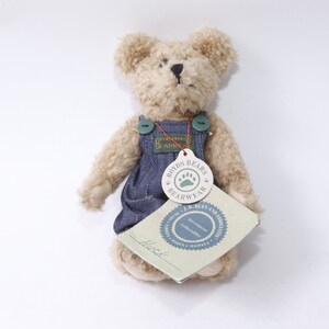 Puede incluir: Un oso de peluche beige con un mono vaquero azul con un botón verde. El oso tiene una etiqueta que dice "Boyds Bears Bearwear with J.R. Bean and Associates Investment Collectibles Since 1993".