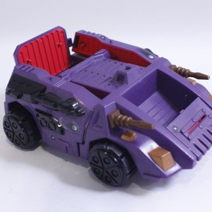 May include: A purple toy vehicle with black wheels and brown accents. The vehicle has a red interior and a hinged back door.