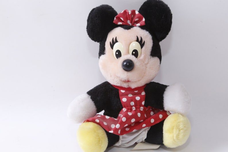K&ouml;nnte beinhalten: Ein Pl&uuml;schtier aus schwarzem und wei&szlig;em Mickey Mouse, das ein rotes Kleid mit wei&szlig;en Punkten und einer roten Schleife tr&auml;gt. Das Spielzeug hat gro&szlig;e schwarze Augen und eine schwarze Nase.