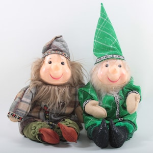 Puede incluir: Dos muñecos enanos de peluche, uno con un gorro de cuadros verdes y ropa de cuadros verdes, el otro con un gorro de cuadros marrones y ropa de cuadros marrones.