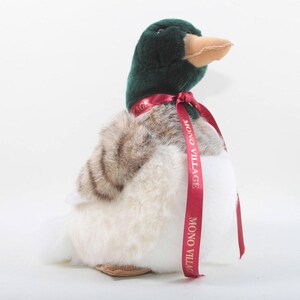May include: A plush duck toy with a green head, tan beak, and a red ribbon around its neck. The duck has a white chest and brown and white striped wings. The ribbon has the text "MONO VILLAGE".