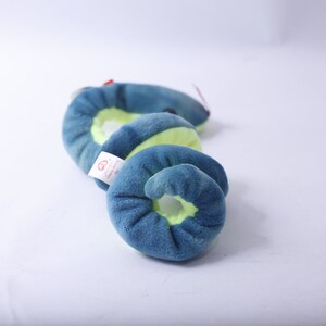 Pode incluir: Um brinquedo de pel&uacute;cia azul e verde em forma de cobra. A cobra est&aacute; enrolada em espiral. O brinquedo tem uma pequena etiqueta vermelha anexada.