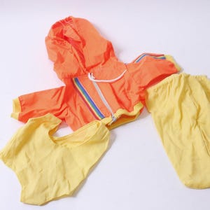 May include: A bright orange hooded jacket with a rainbow stripe down the zipper and matching yellow pants. The jacket has a zipper closure and a hood.