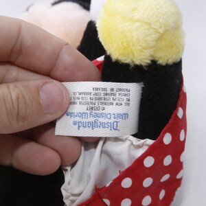 K&ouml;nnte beinhalten: Ein rotes und wei&szlig;es gepunktetes Stoff-Minnie-Maus-Pl&uuml;schtier mit schwarzem K&ouml;rper und gelbem Kopf. Das Etikett lautet "Disneyland Walt Disney World DISNEY All New Materials Polyester Fiberfill HE 1525 PA 1374:CHIO PA 1378 HASS T CARISE TRADING CORP. BURBARE, CA PRODUCT OF SRILANKA"