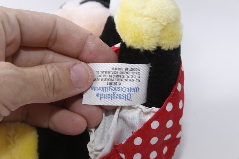 K&ouml;nnte beinhalten: Ein rotes und wei&szlig;es gepunktetes Stoff-Minnie-Maus-Pl&uuml;schtier mit schwarzem K&ouml;rper und gelbem Kopf. Das Etikett lautet "Disneyland Walt Disney World DISNEY All New Materials Polyester Fiberfill HE 1525 PA 1374:CHIO PA 1378 HASS T CARISE TRADING CORP. BURBARE, CA PRODUCT OF SRILANKA"