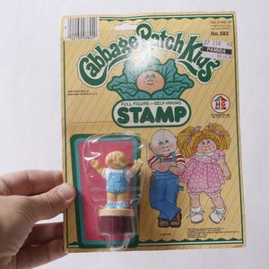 May include: A vintage Cabbage Patch Kids full figure self-inking stamp. The packaging features the Cabbage Patch Kids logo and illustrations of the dolls. The stamp is in a clear plastic casing. The stamp is a collectible item.