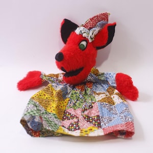 May include: A handmade red fox puppet with black ears and a smiling mouth. The puppet's body is a patchwork of colorful fabric squares. The fox has red fur on its head and arms, and green eyes.