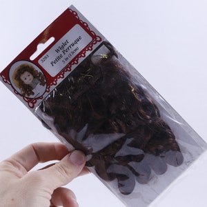 May include: A package of brown wiggler doll hair, labeled "Wiggler Petite Perruque 5 in (13 cm)".