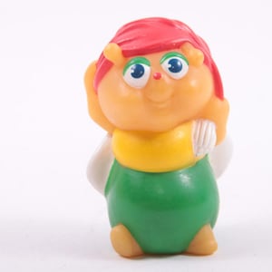 Könnte beinhalten: Vintage Kunststoff-Spielfigur einer Zeichentrickfigur mit rundem, orangefarbenem Körper. Sie hat rotes Haar, blaue Augen und ein gelbes Oberteil mit grüner Hose. Die Figur hat weiße Flügel und steht.