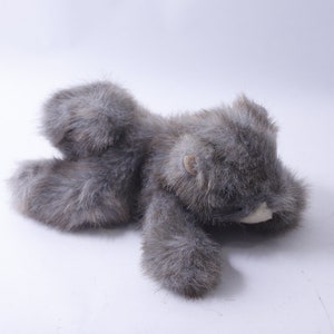 May include: A gray plush toy bear lying on its side with its head resting on its paw. The bear has a soft, furry texture and a white nose.