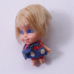 May include: A vintage doll with blonde hair and blue eyes. The doll is wearing a red and blue outfit with white polka dots. The doll's arms are outstretched, and it has a smiling expression.