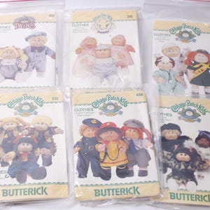 Könnte beinhalten: Eine Sammlung von Vintage-Schnittmustern für Cabbage Patch Kids-Kleidung in versiegelter Kunststoffverpackung. Die Muster zeigen Illustrationen der Puppen in verschiedenen Outfits, mit dem Butterick-Markenlogo.