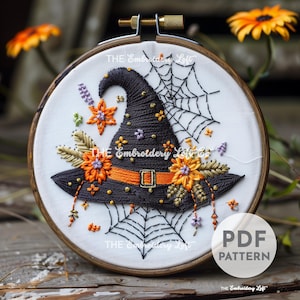 Puede incluir: Sombrero de bruja bordado con flores naranjas, negras y moradas, una telaraña negra y el texto "THE Embroidery Loft Co."