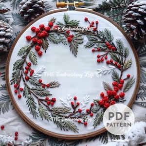 May include: A white embroidery hoop with a green and red floral wreath design. The wreath is made of green leaves and red berries. The text "THE Embroidery Loft Co." is written on the hoop. The text "PDF PATTERN" is written in the lower right corner of the hoop.