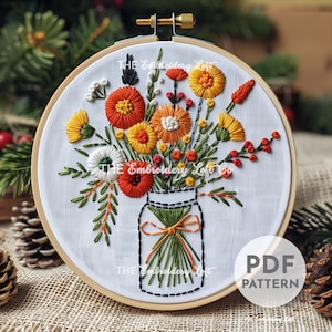 May include: A circular wooden embroidery hoop containing white fabric with a hand-stitched floral bouquet in a mason jar. The design features orange, yellow, and white flowers with green stems and leaves. The text "THE Embroidery Loft Co" and "PDF PATTERN" are visible.
