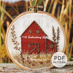 Könnte beinhalten: Stickerei-Hoop-Kunst mit einem roten Scheunenhaus mit brauner Tür und Fenstern, umgeben von braunem und goldenem gesticktem Gras und Weizenhalmen. Der Hoop ist mit "THE Embroidery Loft Co." beschriftet.