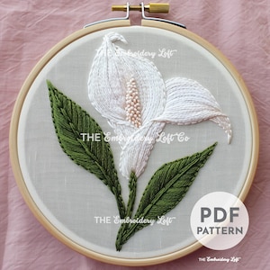 May include: White embroidery hoop with a white flower with green leaves. The text "THE Embroidery Loft Co." is visible in the image. The text "PDF PATTERN" is also visible in the image.