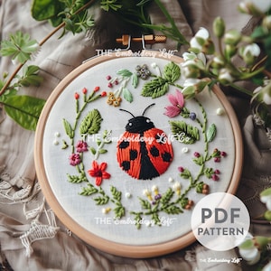 May include: Embroidery pattern featuring a red ladybug with black spots surrounded by green leaves and pink and white flowers. The pattern is in a hoop and the text "PDF PATTERN" is visible in the lower right corner.