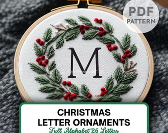 May include: A white embroidery hoop with a green and red Christmas wreath design. The letter "M" is embroidered in the centre of the wreath. The text "PDF PATTERN" is in the top right corner of the image. The text "CHRISTMAS LETTER ORNAMENTS Full Alphabet 26 Letters" is at the bottom of the image.