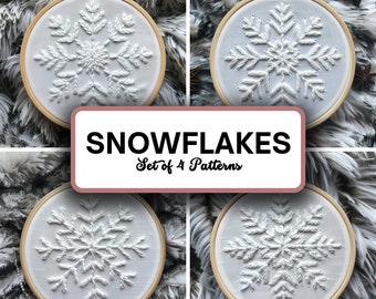 May include: Four white embroidery hoops with snowflake designs. The hoops are on a fluffy white background. The text "SNOWFLAKES Set of 4 Patterns" is in a pink rectangle.