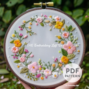 May include: A PDF pattern for embroidery featuring a floral wreath with pink, yellow, and green flowers. The pattern is displayed in a wooden embroidery hoop.
