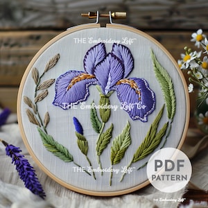 Può includere: Fiore di iris ricamato in un cerchio di legno. L'iris viola ha accenti dorati e foglie verdi. Il testo "THE Embroidery Loft" e "PDF PATTERN" sono visibili. Il ricamo è su un tessuto grigio chiaro.