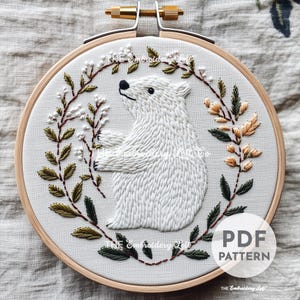 May include: Embroidered hoop art featuring a white polar bear surrounded by a wreath of green and yellow leaves. The text "PDF PATTERN" is in the lower right corner of the hoop.