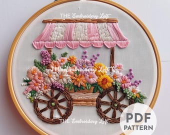 May include: Embroidered hoop art featuring a flower cart with a pink striped awning. The cart is filled with colorful flowers and has wooden wheels. The text "THE Embroidery Loft" appears three times on the hoop.