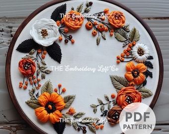 Puede incluir: Un aro de bordado blanco con un diseño de corona de flores. La corona está hecha de hilo de bordar naranja, blanco y verde. El texto "THE Embroidery Loft Co" es visible en el centro del aro. El texto "PDF PATTERN" es visible en la esquina inferior derecha del aro.