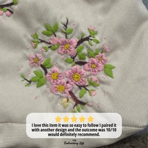 Pode incluir: Um close-up de um tecido branco com flores bordadas de rosa. O tecido tem uma superf&iacute;cie texturizada. O texto "I love this item it was so easy to follow I paired it with another design and the outcome was 10/10 would definitely recommend. THE Embroidery Loft" &eacute; vis&iacute;vel na parte inferior da imagem.
