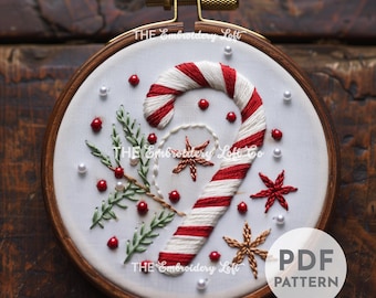 May include: A white embroidery hoop featuring a red and white candy cane, green holly sprigs, red berries, white pearls, and gold and red star-shaped embroidery designs. The text "THE Embroidery Loft Co" is visible in the image. The text "PDF PATTERN" is also visible in the image.