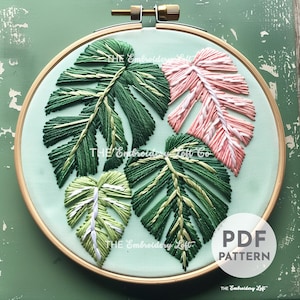 Op de afbeelding: Een PDF-patroon voor borduurwerk met een hoepel met vier bladeren, twee groen, één roze en één wit en groen. De bladeren zijn geborduurd met verschillende borduurtechnieken. De tekst "PDF PATTERN" is op de hoepel gedrukt.