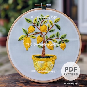 May include: Embroidered lemon tree design in a yellow pot on a white fabric background. The design is in a hoop and includes the text "THE Embroidery Loft Co."