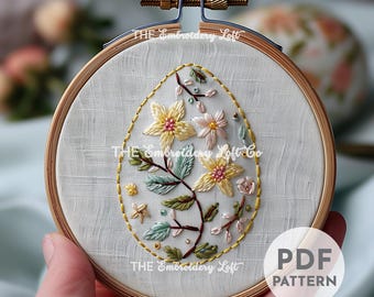 May include: Embroidered floral design in a white hoop with a light wood frame. The design features a branch with yellow, pink, and green flowers. The text "THE Embroidery Loft Co" is visible in the image.