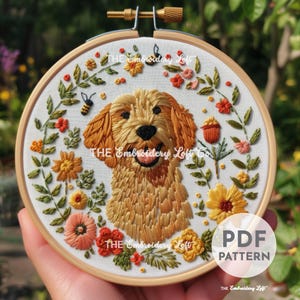 May include: Embroidered hoop art featuring a golden doodle dog with a smiling expression, surrounded by colorful flowers and greenery. The text "THE Embroidery Loft" is visible. A "PDF PATTERN" label is also present.