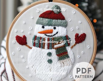 May include: Embroidered snowman with a red and green hat, scarf, and mittens. The snowman is surrounded by white dots on a white background. The embroidery is in a hoop with a wooden frame. The text "PDF PATTERN" is in the lower right corner of the image.