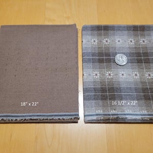 May include: Two rectangular fabric pieces, one solid brown, the other patterned with a plaid and floral design. The solid piece measures 45.7 x 55.9 cm, and the patterned piece is 41.9 x 55.9 cm. A coin rests on the patterned fabric.