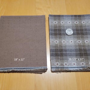 May include: Two rectangular fabric pieces, one solid brown, the other patterned with a plaid design in brown, grey, and white. The solid piece measures 45.7 x 55.9 cm. The patterned piece is 41.9 x 55.9 cm. A coin rests on the patterned fabric.