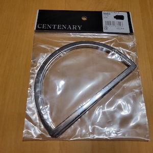 May include: A silver-colored, semi-circular metal frame, packaged in a clear plastic bag. The frame has a flat, straight edge and a rounded top. The packaging includes the word "CENTENARY" and other text.
